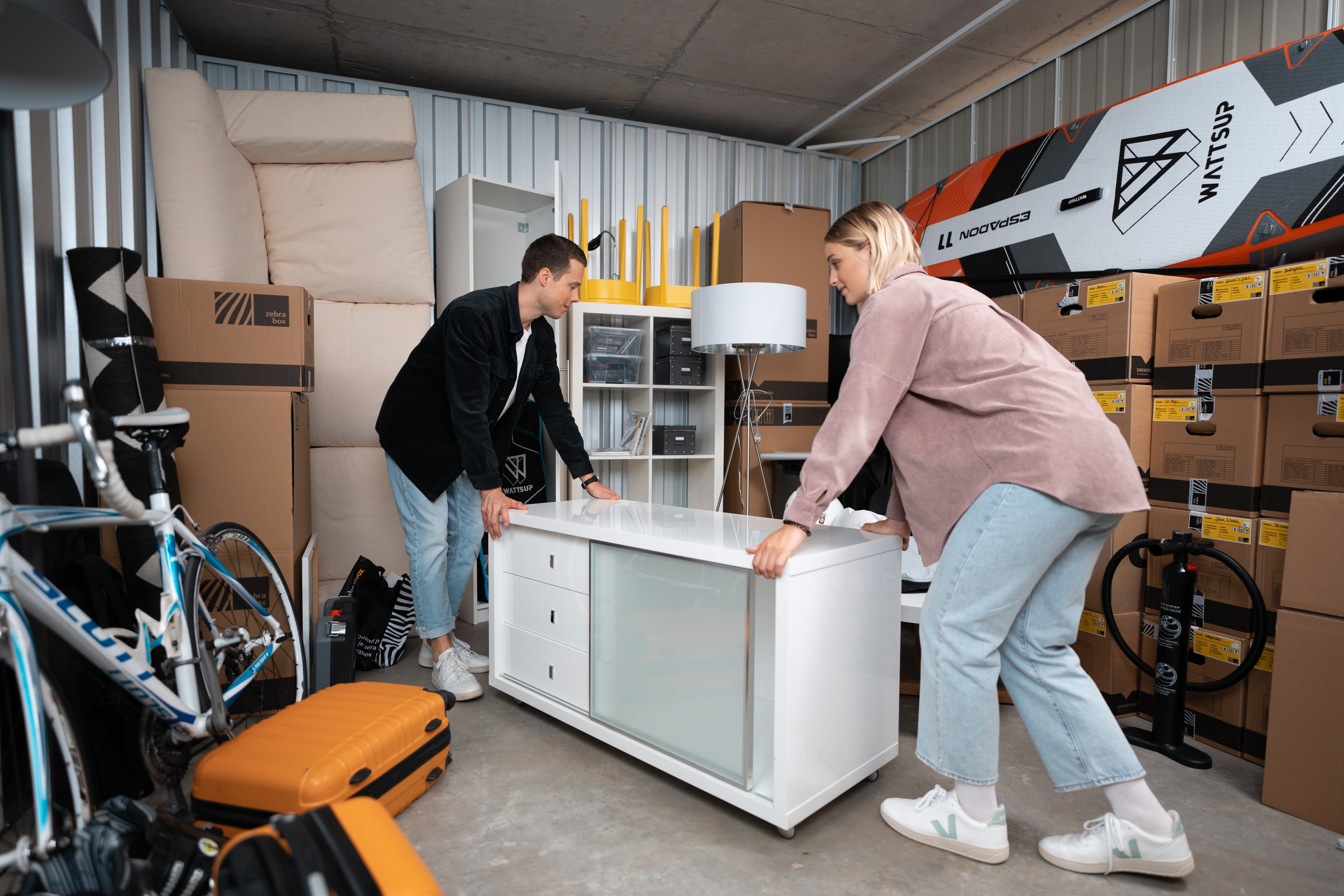 Ein junges Paar rollt ein Sideboard in den Lagerraum von Zebrabox.