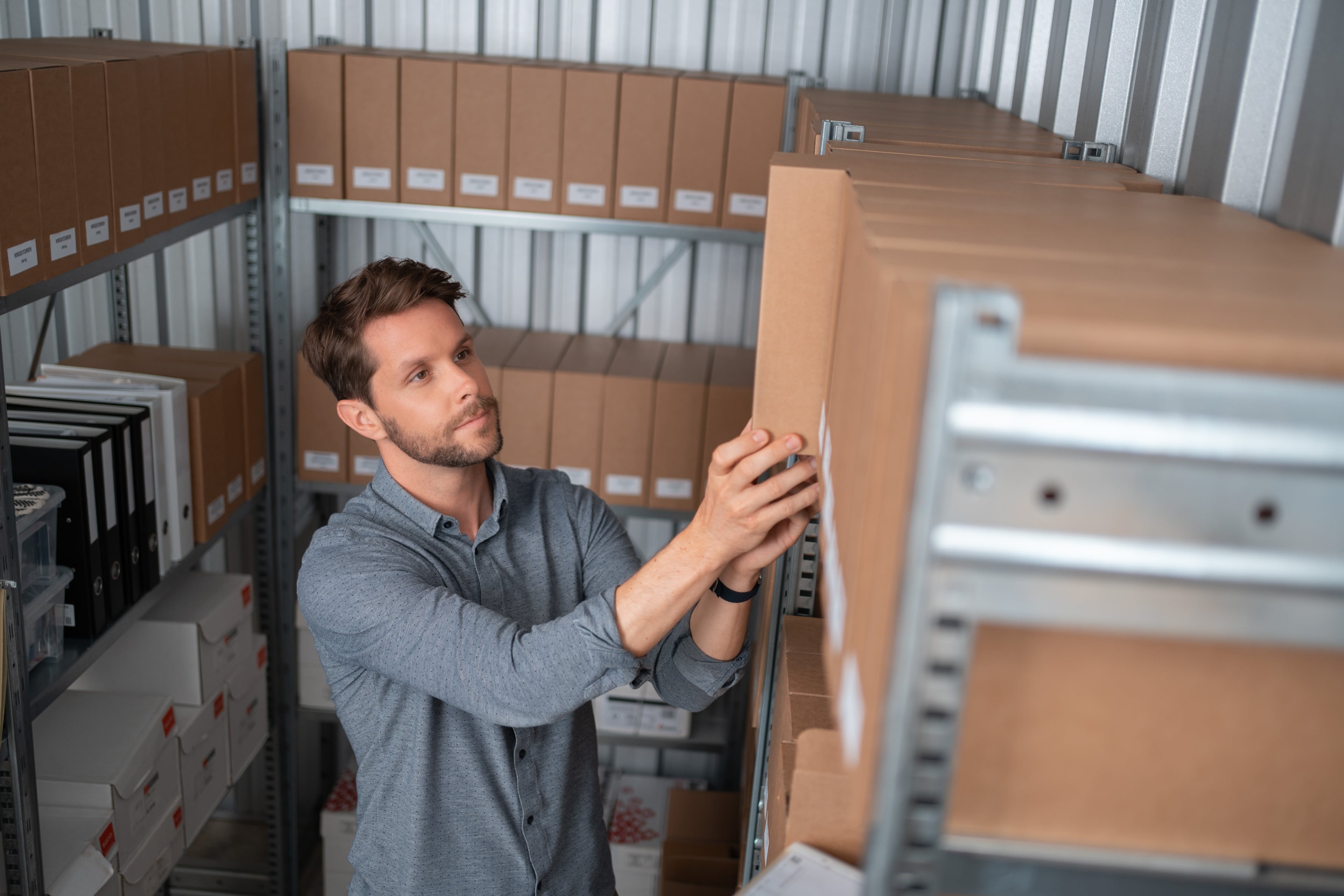 Un homme se tient dans l'entrepôt de l'entreprise Zebrabox et place une boîte d'archives sur une étagère emboîtable.