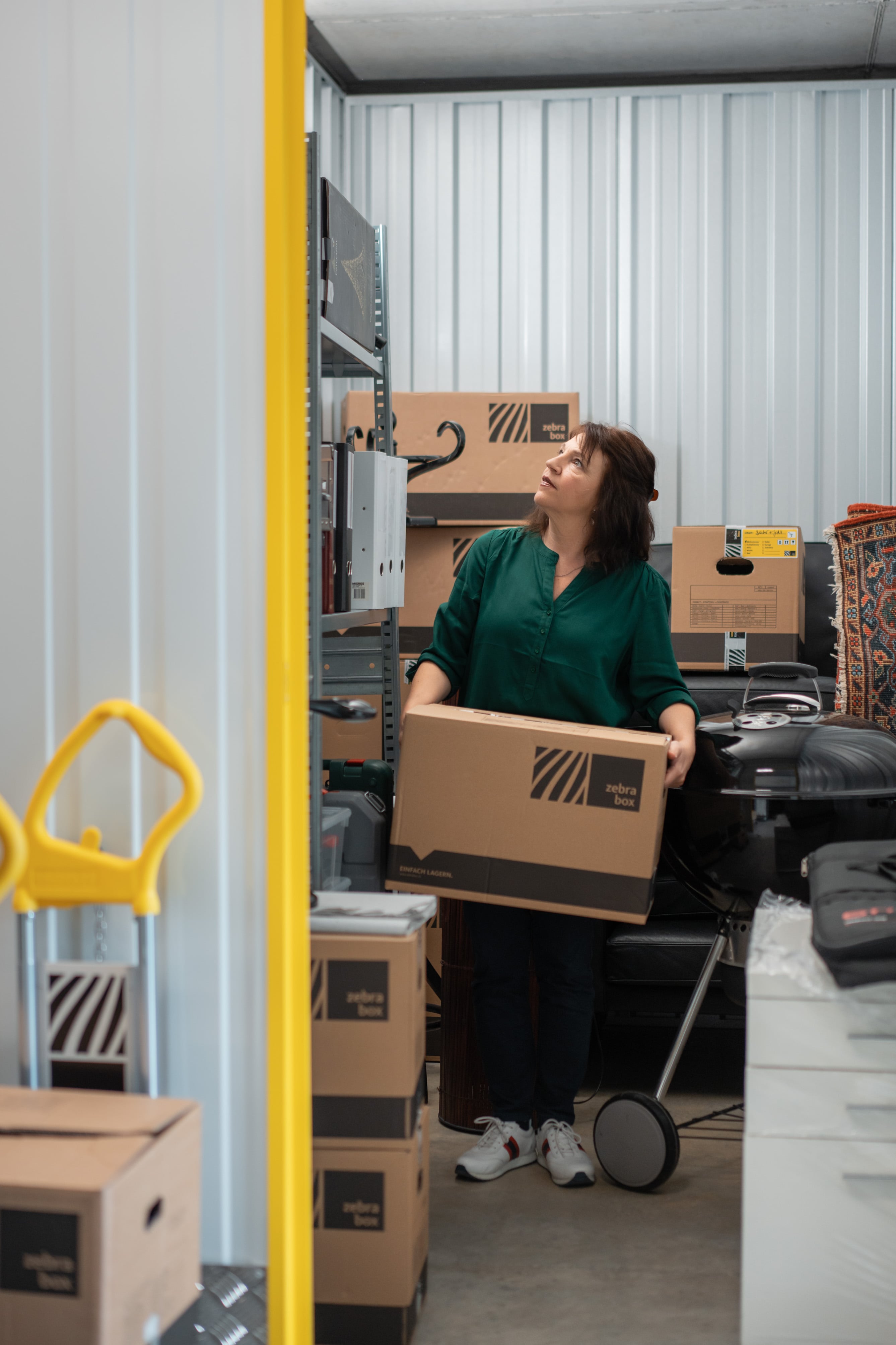 A middle-aged woman is storing a moving box in her storage unit at Zebrabox.