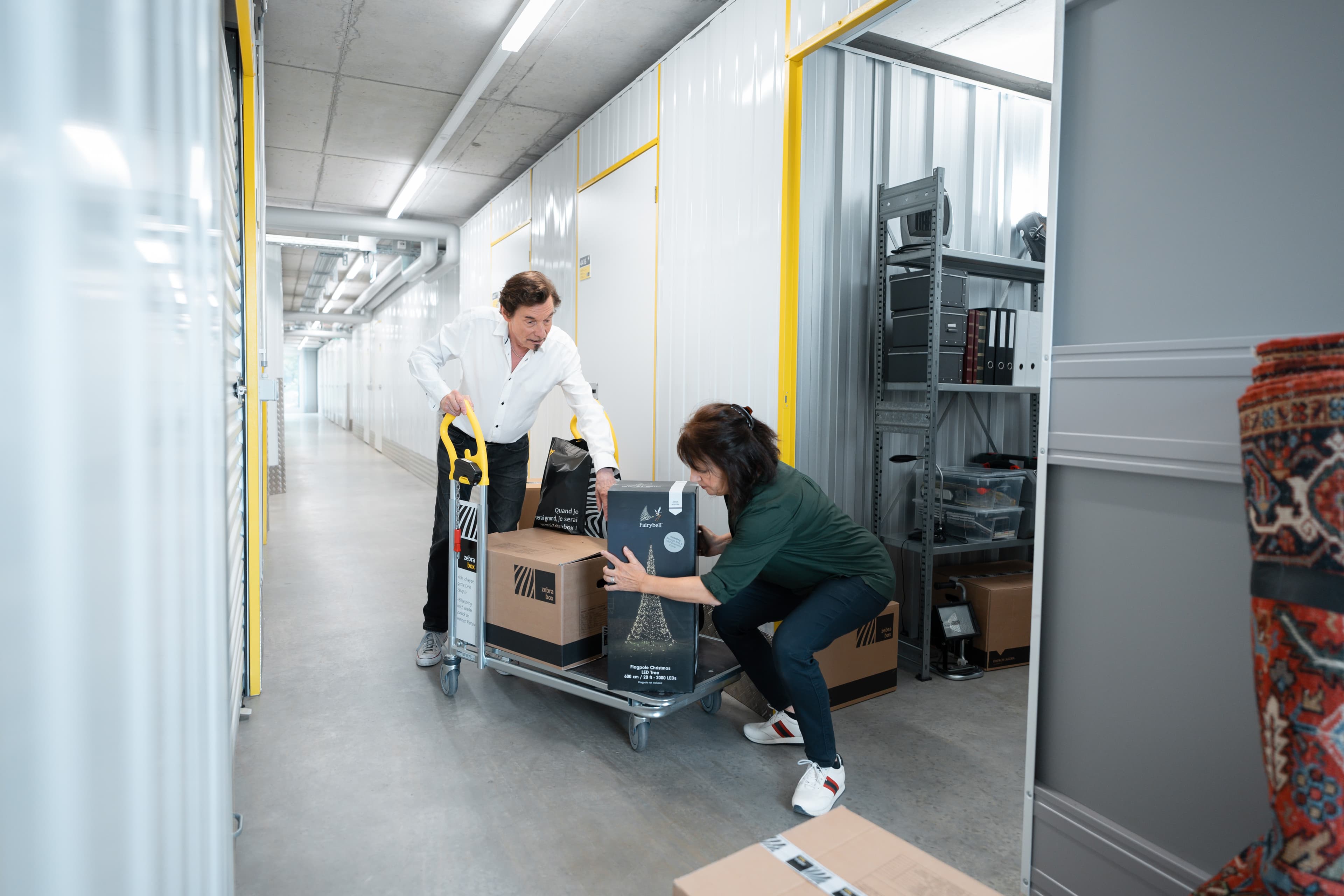 An elderly couple is unloading a filled trolley and is storing items in the storage unit at Zebrabox.