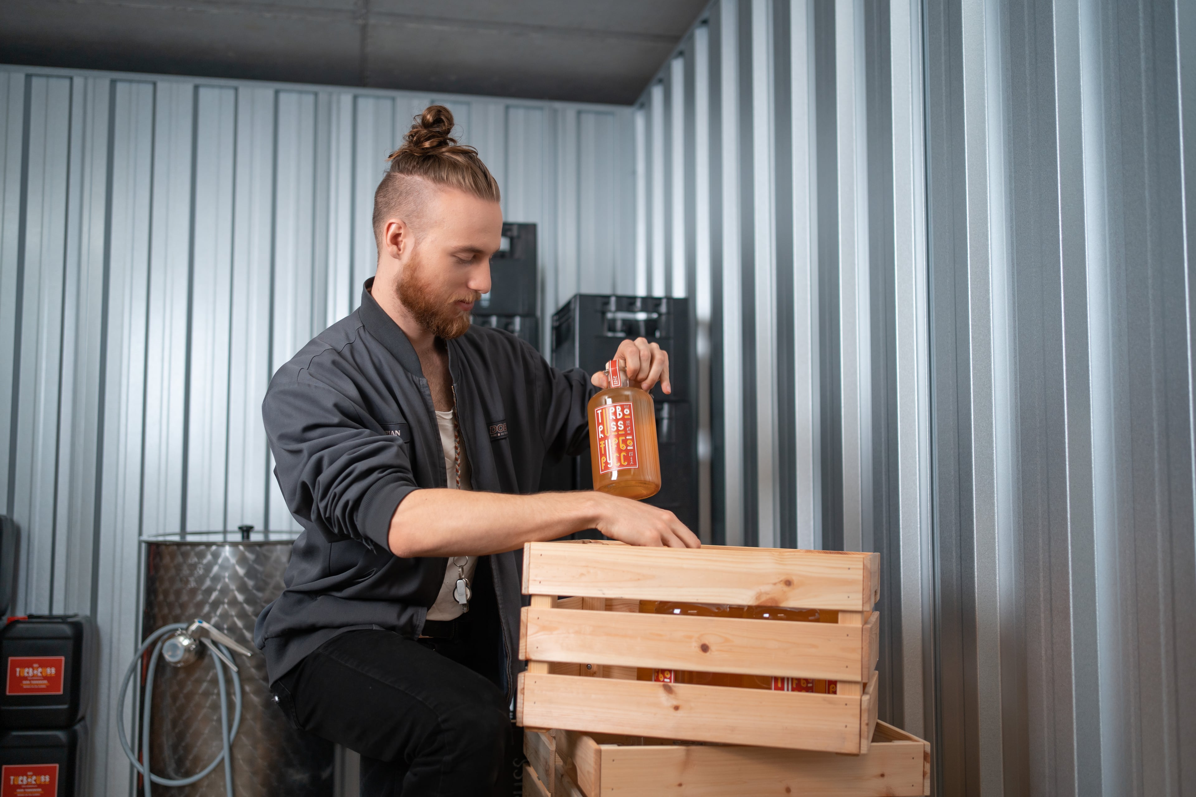 A young man is standing in the warehouse at Zebrabox and storing a bottle in a wooden crate.