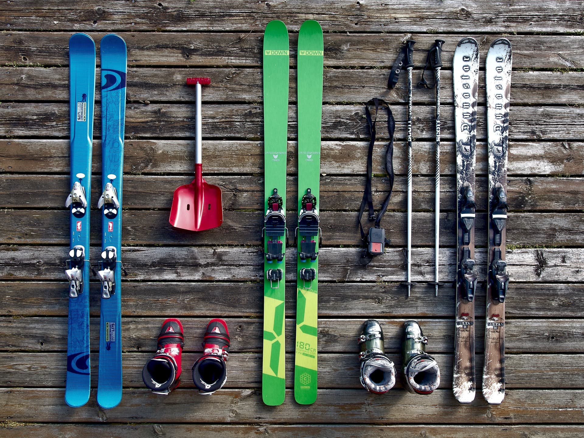 Bird's eye view of three pairs of skis with ski boots, ski poles and avalanche rescue equipment.