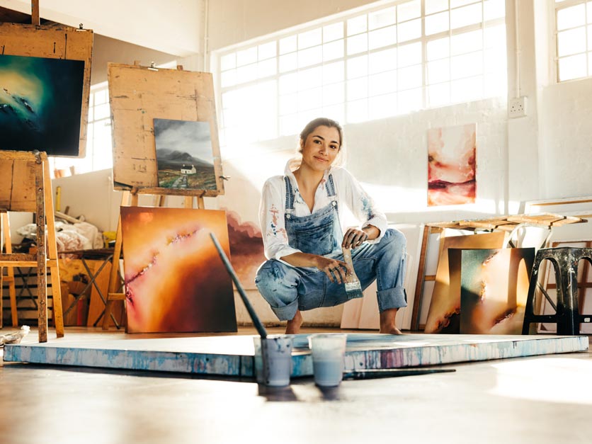 Young artist posing in front of her paintings