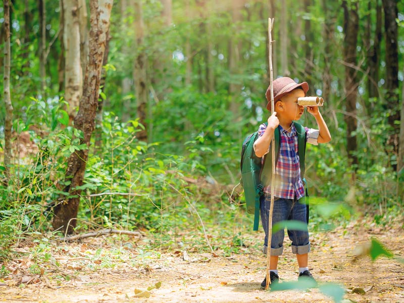 Un garçon regarde à travers des jumelles dans la forêt